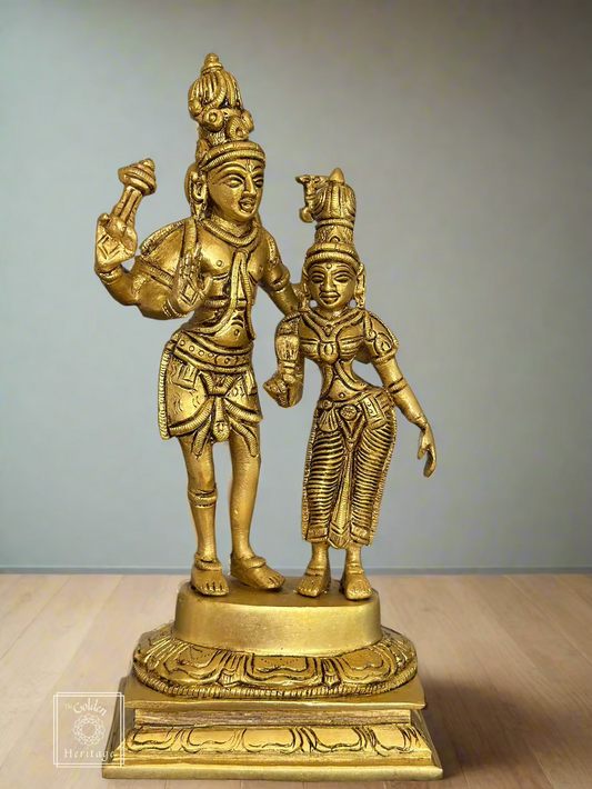 A gold brass statue of the Hindu gods Shiva and Parvati, depicting them in a standing pose with their hands raised. The statue is intricately designed with detailed patterns and has a glossy finish.