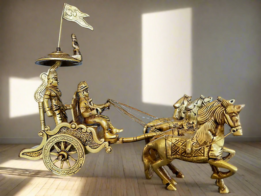 A brass sculpture of the Krishna Arjuna chariot with four horses, depicting a scene from the Mahabharata. The sculpture is intricately detailed, showing the characters in mid-battle pose with the divine being Krishna on the chariot.