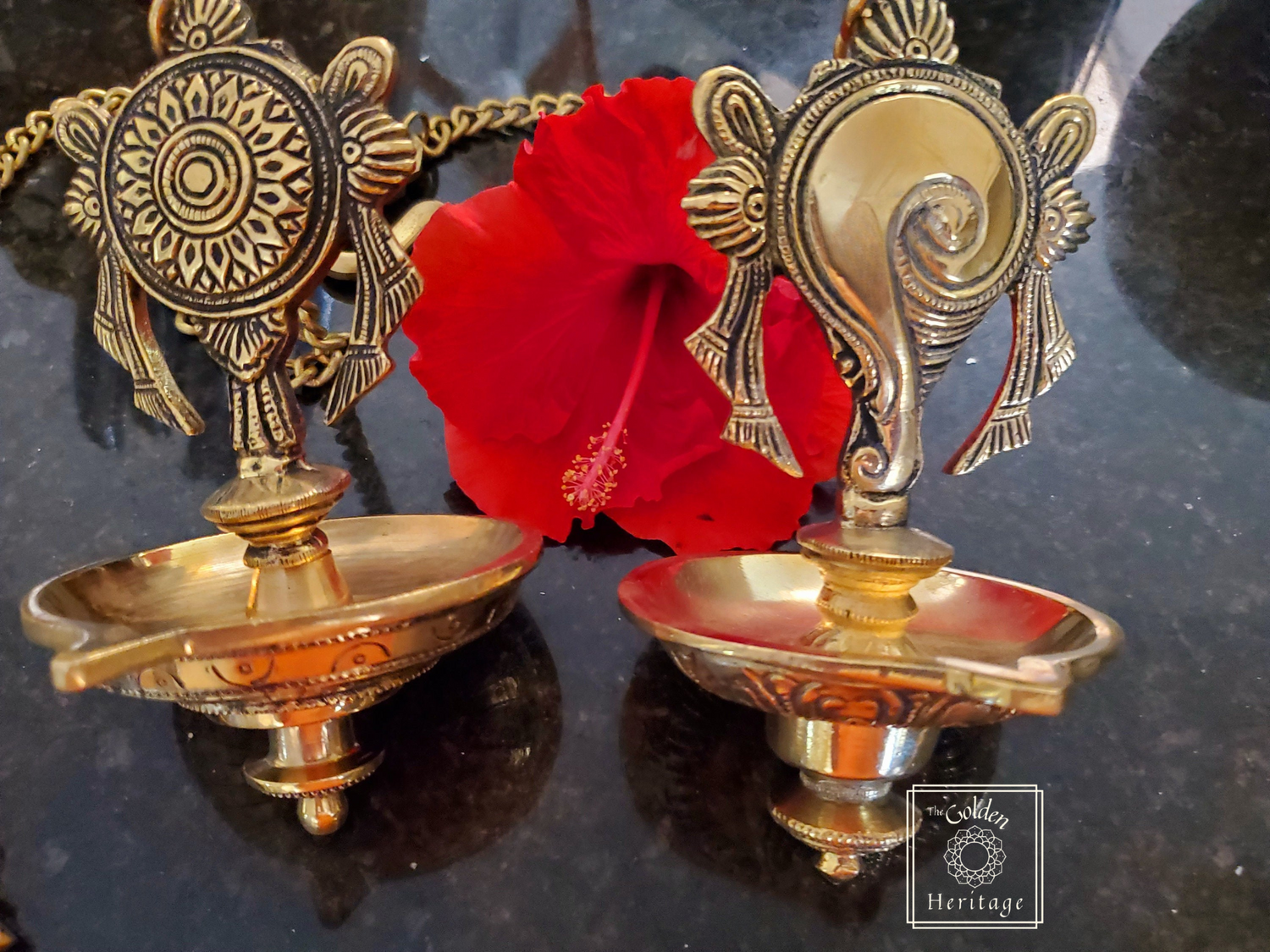 Two brass lamps with intricate designs, featuring symbols resembling a conch shell and a chakra.