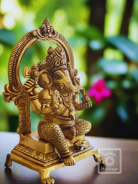 A brass statue of Lord Ganesha with intricate details, seated and holding a Modak