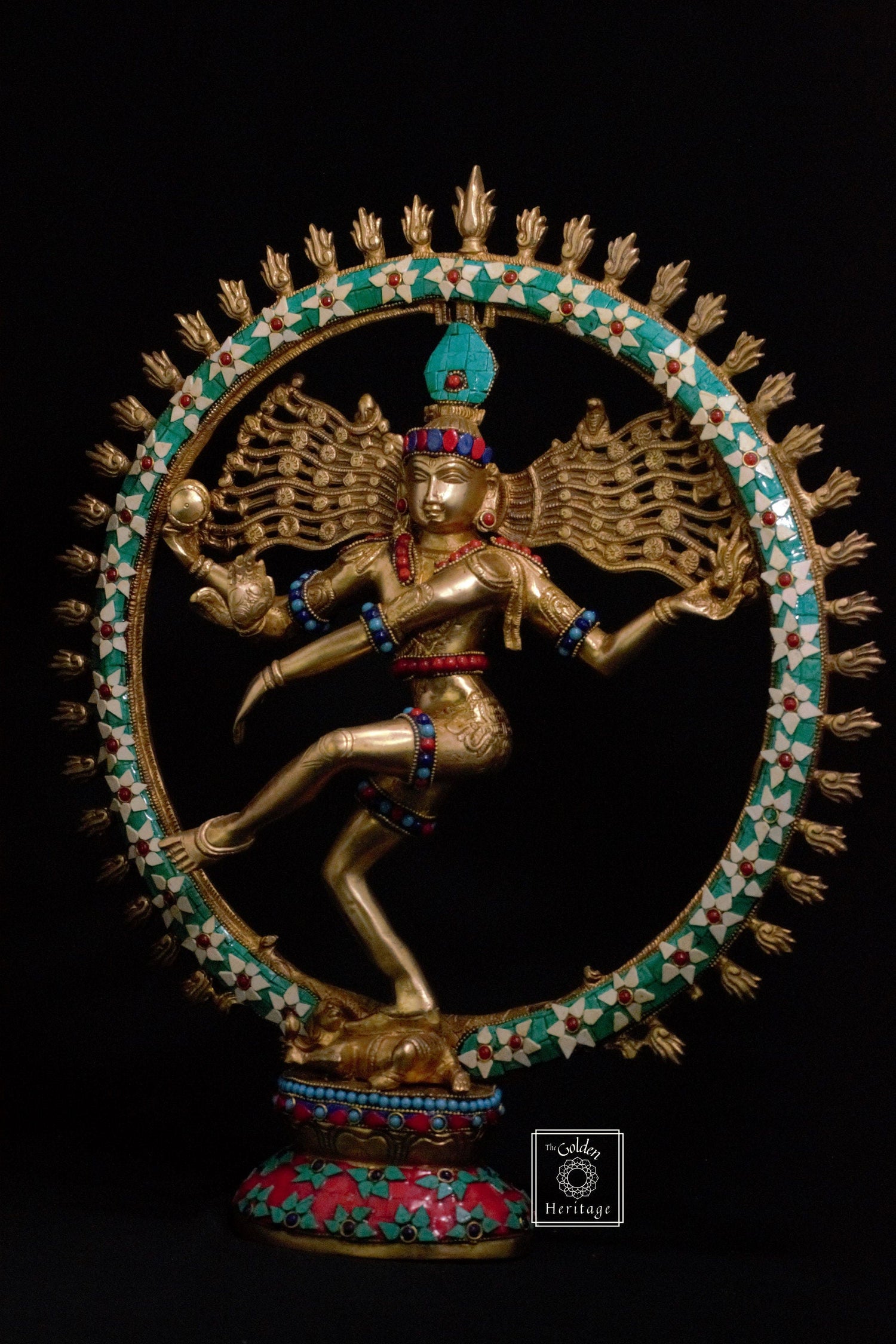 A brass statue of Lord Shiva as Nataraja, the cosmic dancer, with a halo of flames, adorned with stonework and a radiant antique finish.