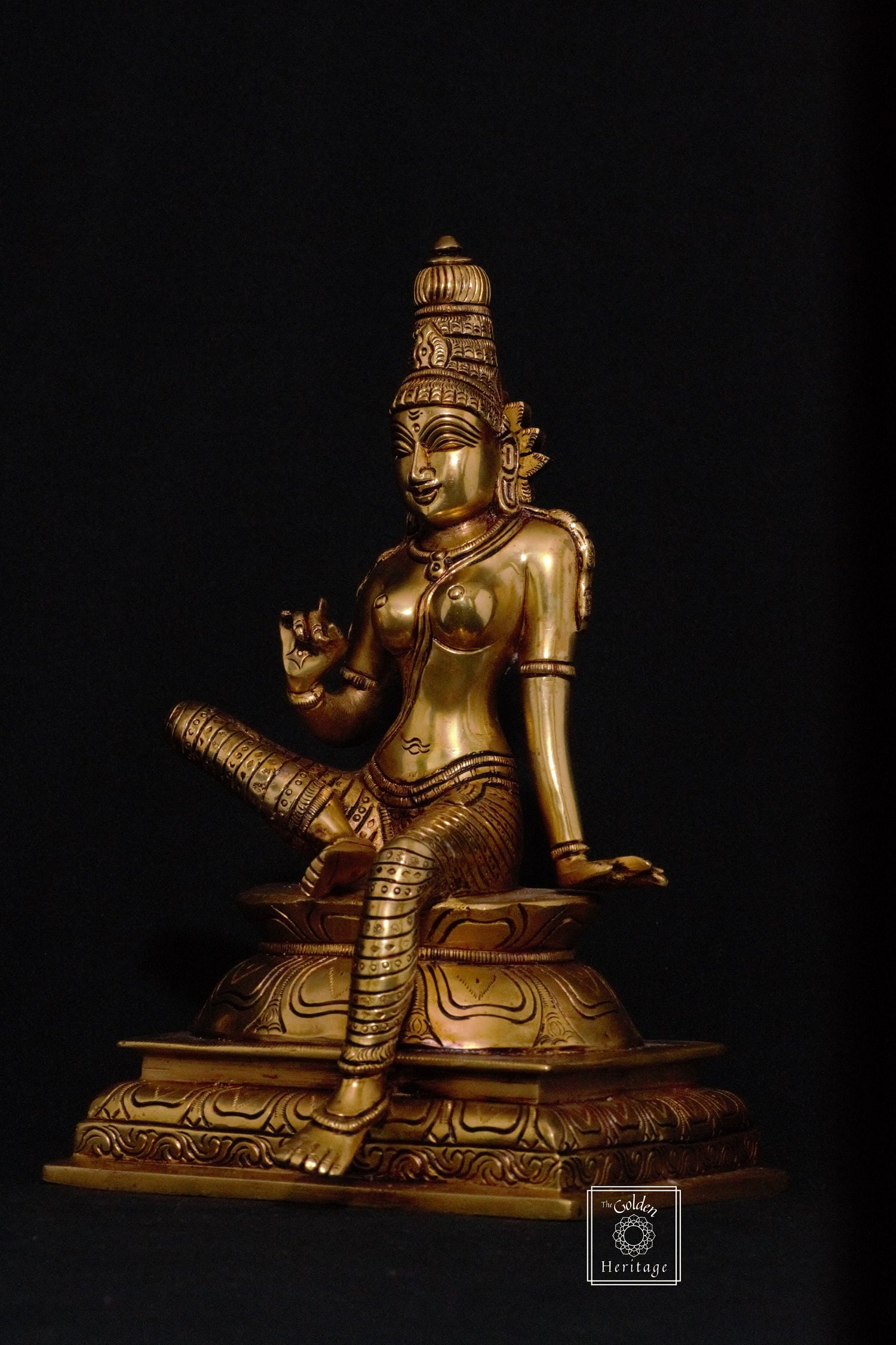 A brass statue of the Hindu goddess Parvati sitting on a throne, holding a vessel and a flower.